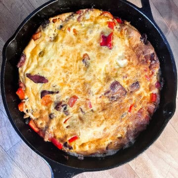 Golden cast iron breakfast frittata with bacon, red bell peppers, and melted cheddar cheese in a Lodge skillet