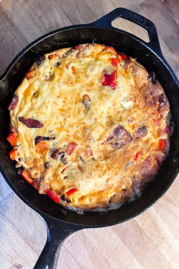 Golden cast iron breakfast frittata with bacon, red bell peppers, and melted cheddar cheese in a Lodge skillet