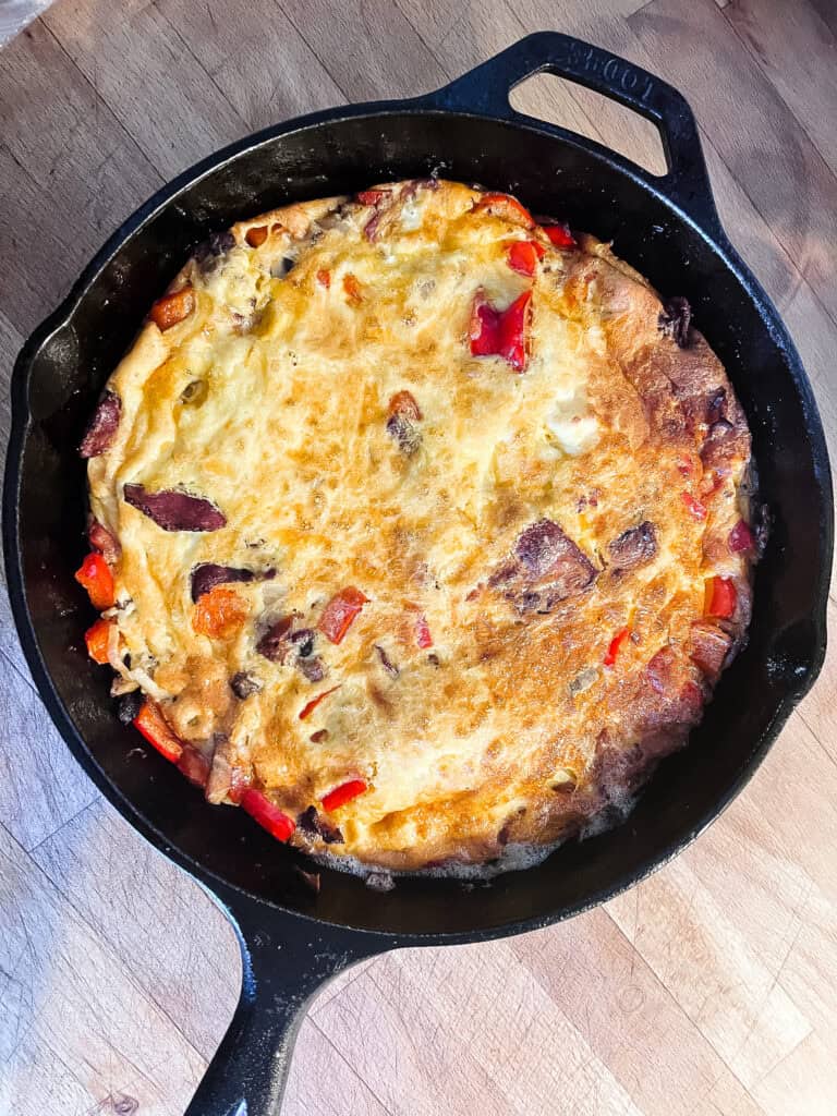 Golden cast iron breakfast frittata with bacon, red bell peppers, and melted cheddar cheese in a Lodge skillet