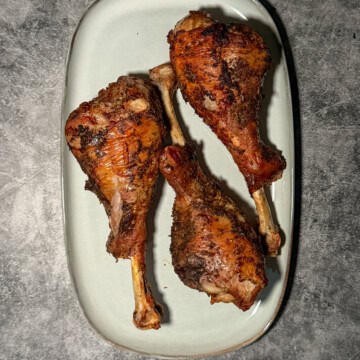 Crispy golden brown air fryer turkey drumsticks on a white plate with herb butter and fresh herbs