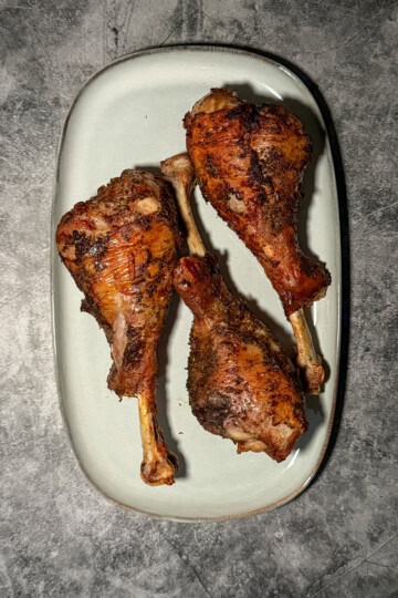 Crispy golden brown air fryer turkey drumsticks on a white plate with herb butter and fresh herbs