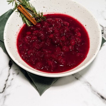 Cranberry sauce with orange in a white bowl topped with fresh rosemary and orange zest