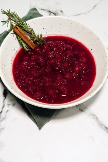 Cranberry sauce with orange in a white bowl topped with fresh rosemary and orange zest
