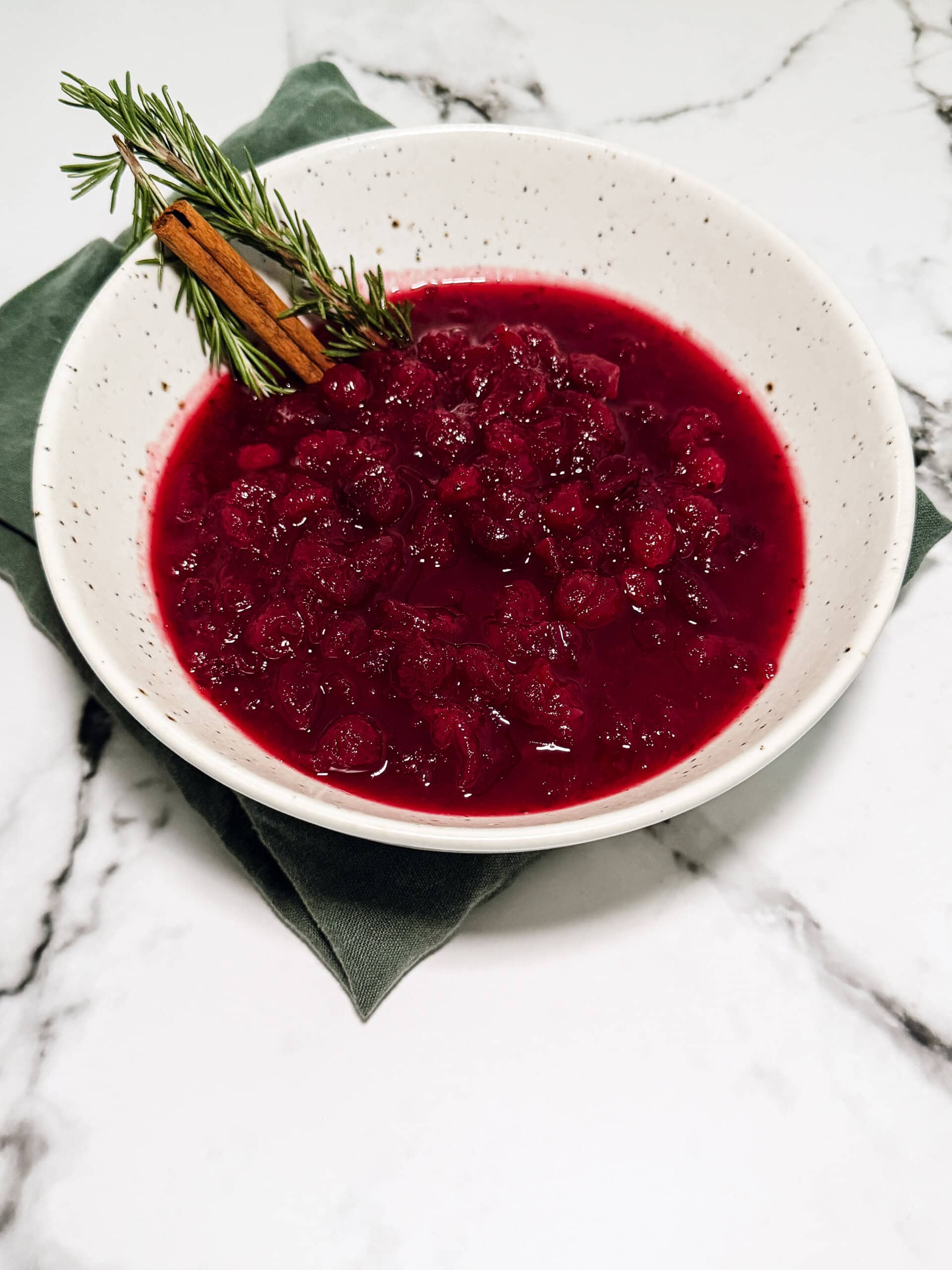 Cranberry sauce with orange in a white bowl topped with fresh rosemary and orange zest