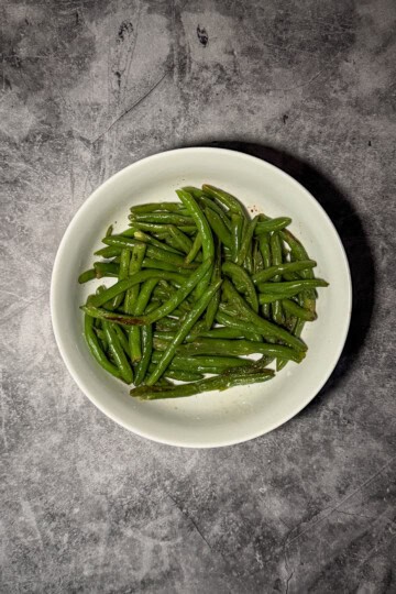 Garlic green beans in a white serving dish with visible garlic pieces and olive oil