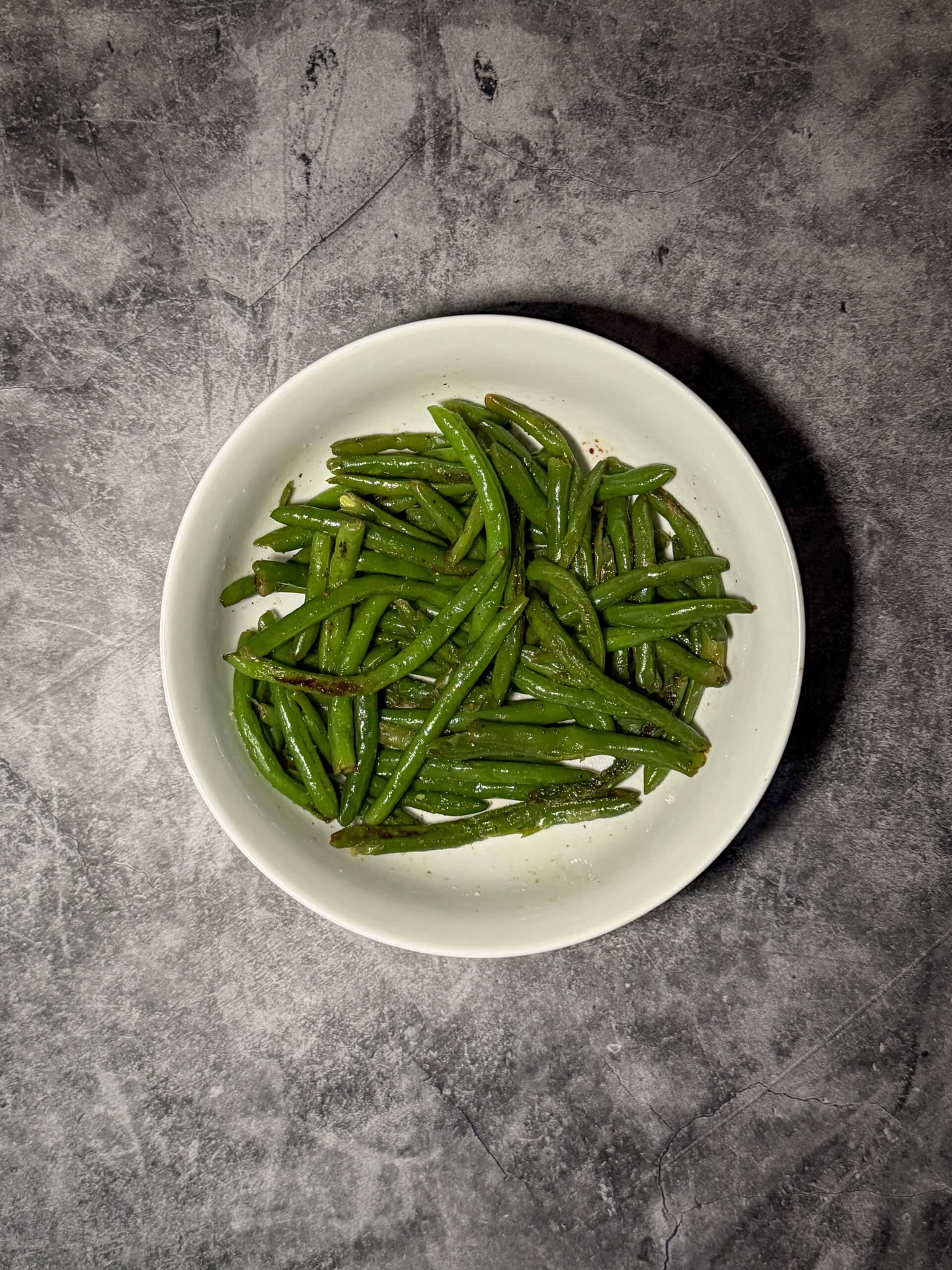 Garlic green beans in a white serving dish with visible garlic pieces and olive oil