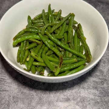 Tender garlic green beans with light char marks in a white ribbed bowl on a gray surface