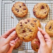 Hands holding thick chocolate chip cookie broken in half showing soft chewy interior and chocolate chunks