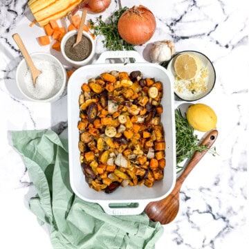 Roasted root vegetables topped with a whole roasted chicken on a baking sheet