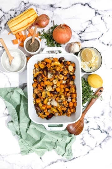Roasted root vegetables topped with a whole roasted chicken on a baking sheet