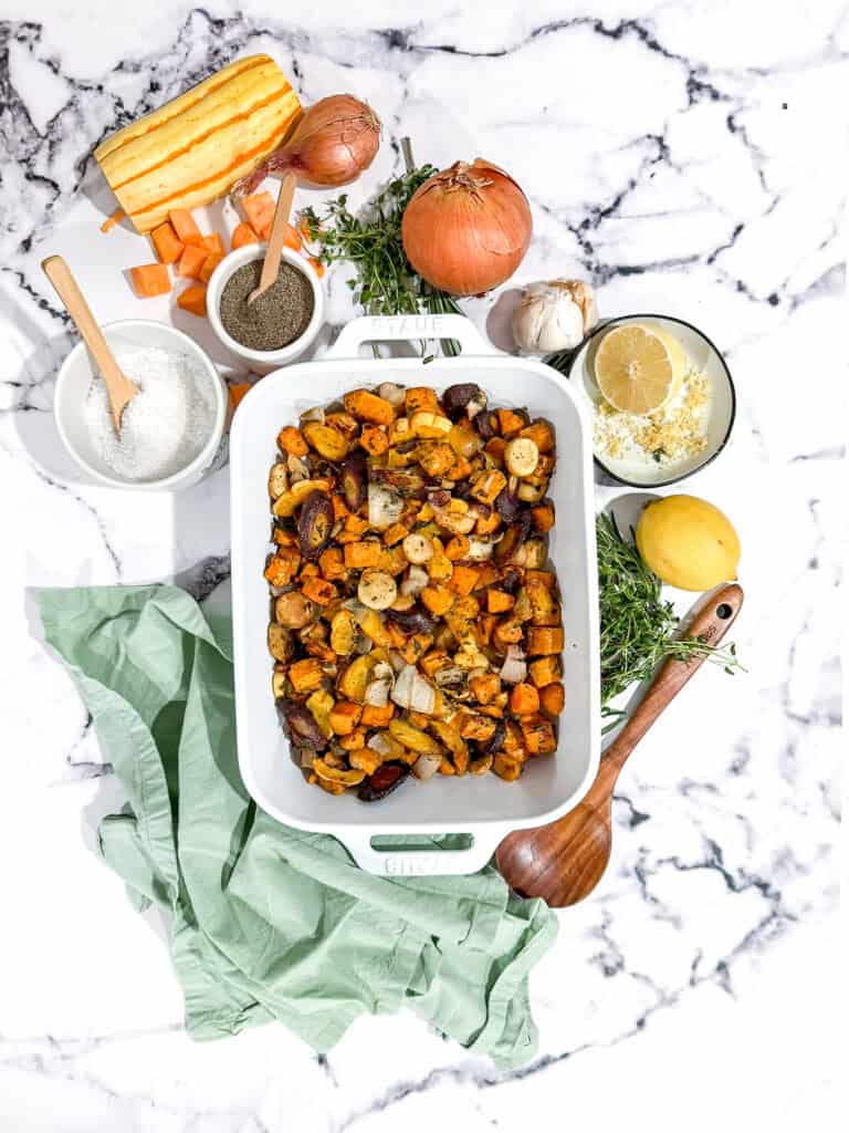 Roasted root vegetables topped with a whole roasted chicken on a baking sheet